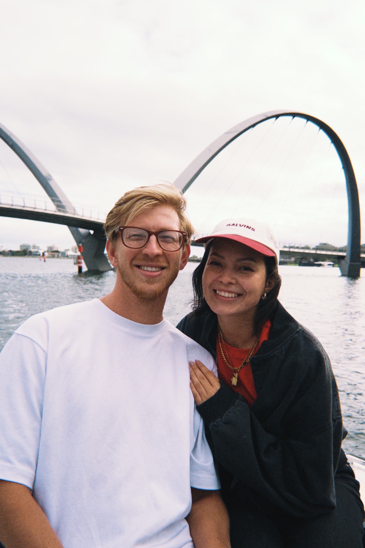 Jono & Monika smiling in front of an arched bridge